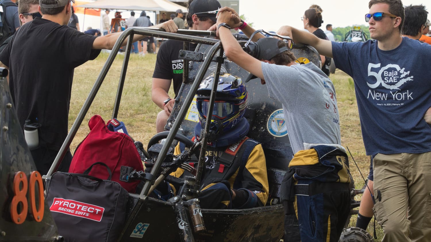 The team gathered around GBR4 in the paddock with the driver seated